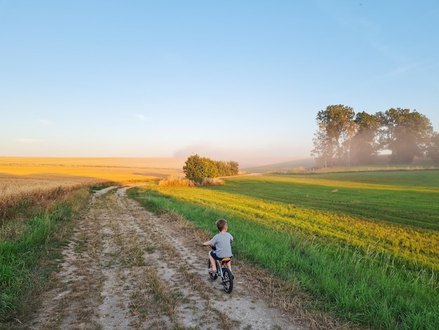 Garotinho andando de bicicleta no campo Andando de pessoa ao pôr do sol na natureza Criança passando seu tempo livre ativa Liberdade bela paisagem Infância feliz