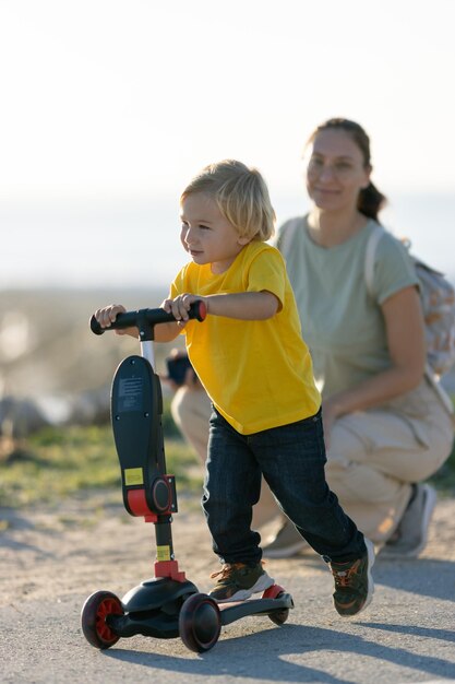 Garotinho andando de scooter e sua mãe olhando para ele