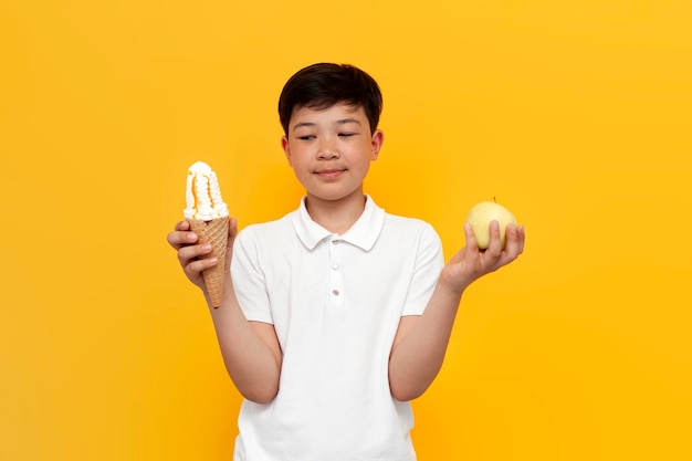 garotinho asiático segurando sorvete e maçã e sobre fundo amarelo garoto coreano