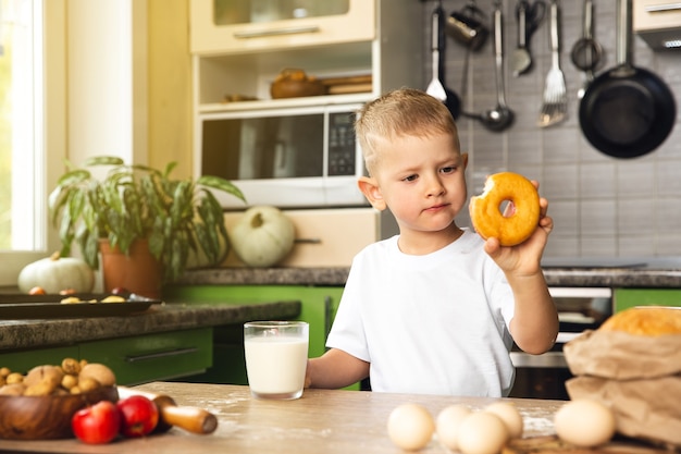 Garotinho bebe leite e come donut na cozinha