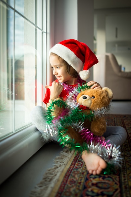 Garotinho bonito boné vermelho de Papai Noel celebra o Natal