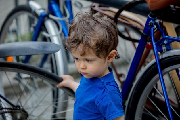 Garotinho brinca com entusiasmo com bicicletas grandes em um estacionamento de bicicletas da cidade