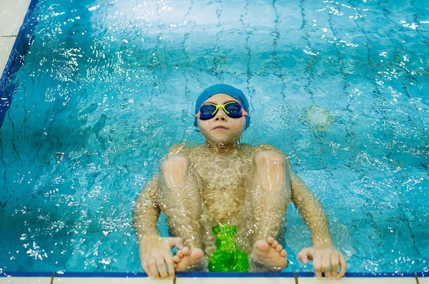 Garotinho caucasiano usando óculos de proteção começa a nadar de costas em uma piscina. Foto de alta qualidade