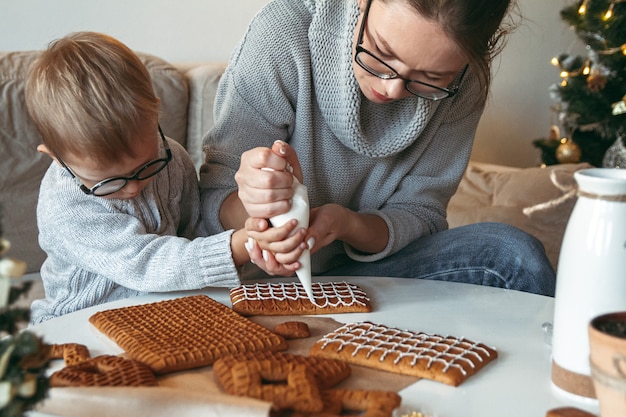 Garotinho com a mãe decorando a casa de pão de mel de natal juntos