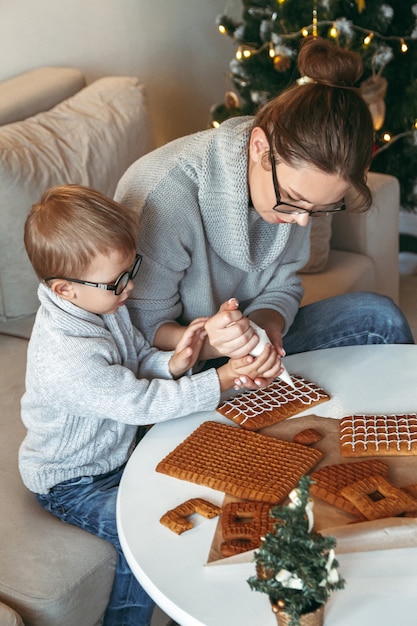 Garotinho com a mãe decorando a casa de pão de mel de Natal juntos