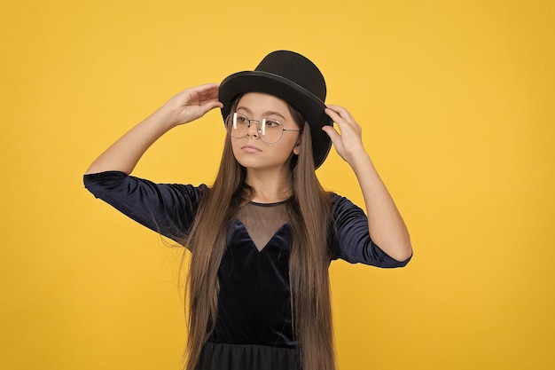 Garotinho com cabelo moreno comprido conserta chapéu preto com festa de moda parece beleza de fundo amarelo