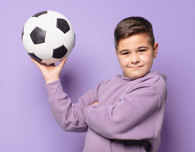 Garotinho com expressão feliz e segurando uma bola de futebol