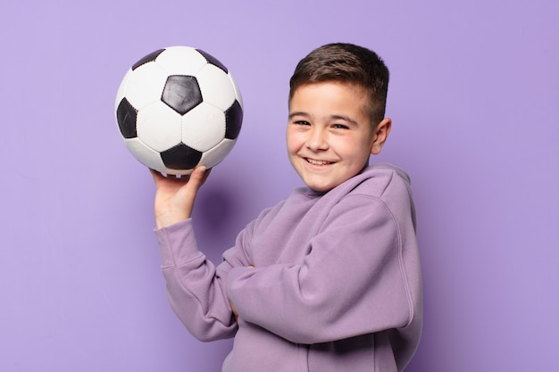 Garotinho com expressão feliz e segurando uma bola de futebol