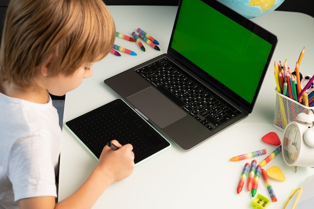 Garotinho com laptop e mesa digitalizadora verde chromakey no laptop