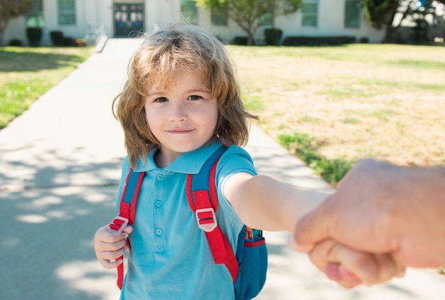 Garotinho com mochila segurando a mão dos pais no fundo do prédio escolar turva Sagacidade infantil