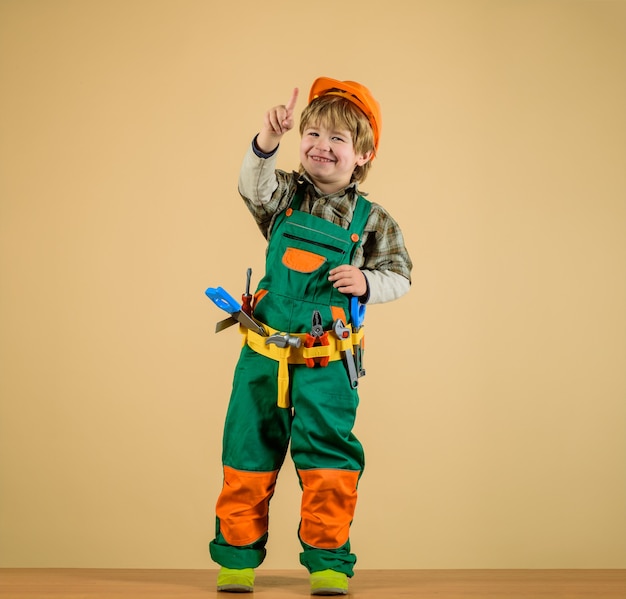 Garotinho com uniforme de construtor com cinto de ferramentas Garoto reparador apontando o dedo para você construtor