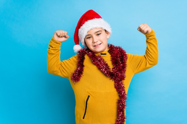 Garotinho, comemorando o dia de Natal, usando um chapéu de Papai Noel isolado mostrando o gesto de força com os braços, símbolo do poder feminino