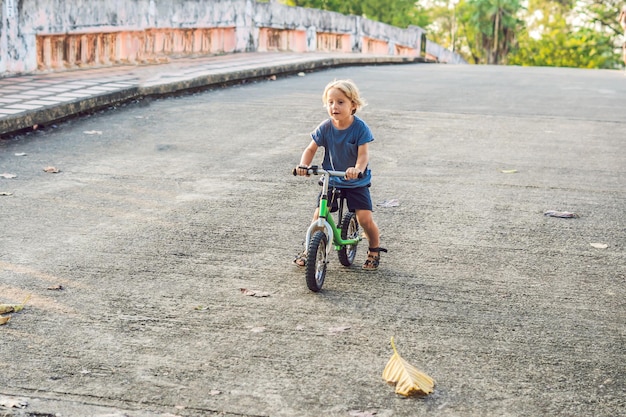 Foto garotinho de bicicleta. pego em movimento, em um movimento de garagem borrado. primeiro dia da criança pré-escolar na bicicleta. a alegria do movimento. o pequeno atleta aprende a manter o equilíbrio enquanto anda de bicicleta