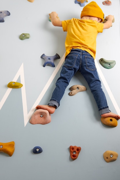 Garotinho de jeans e camiseta amarela escala resolutamente a parede de escalada