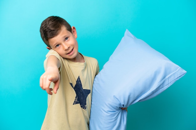 Garotinho de pijama isolado em fundo azul apontando para frente com expressão feliz