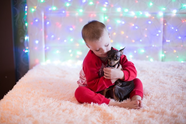 Garotinho de pijama vermelho, brincando com um cachorro na véspera de natal