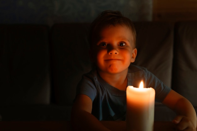 Garotinho de quatro anos admira uma vela acesa de cera à noite em casa