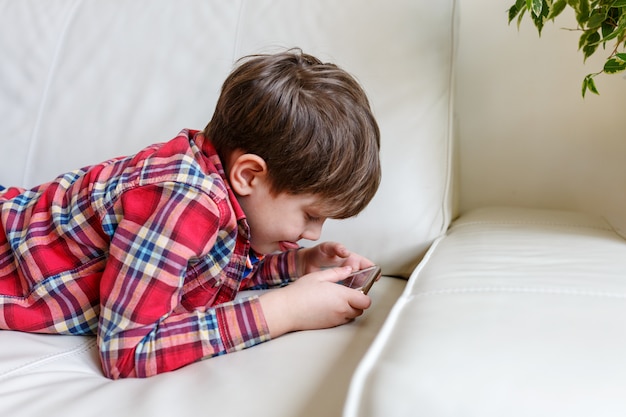 Garotinho deitado na cama jogar telefone inteligente