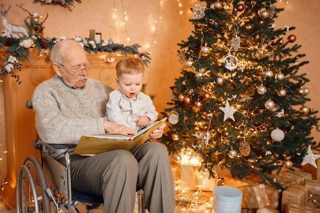 Garotinho e seu velho avô em uma cadeira de rodas sentado perto da árvore de natal