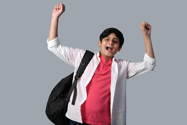 Garotinho em pose frontal usando mochila preta com as mãos levantadas e sorrindo modelo indiano do paquistanês