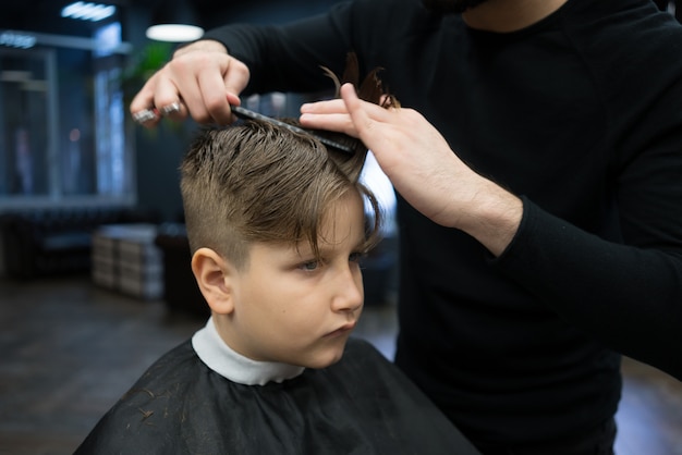 Garotinho em um corte de cabelo no barbeiro se senta em uma cadeira.