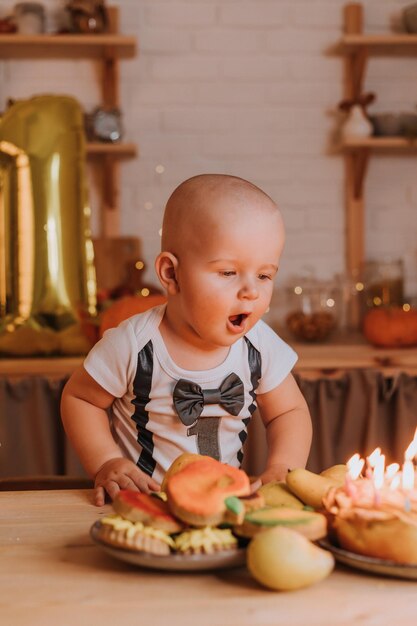 Garotinho em uma camiseta com o número um sopra velas em um bolo de aniversário. primeiro aniversário. Foto de alta qualidade