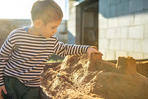 Garotinho está brincando lá fora perto de casa e construindo um castelo de areia