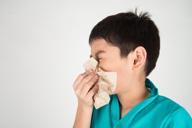 Garotinho está espirrando e tosse da gripe usando o tecido limpo