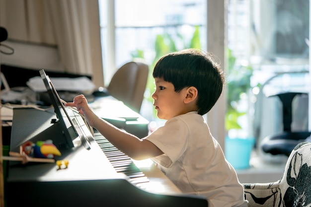 Garotinho está tocando com piano e Music Tablet em casa