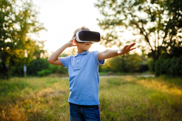 Garotinho fascinado usando óculos de realidade virtual VR. exterior
