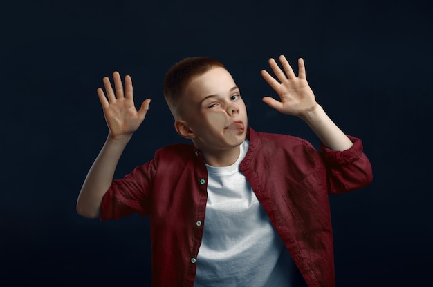 Foto garotinho faz cara encostada no vidro em estúdio. infância feliz, crianças se divertindo, criança engraçada isolada em fundo escuro, emoção infantil