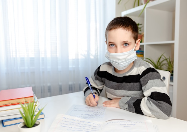 Garotinho fazendo lição de casa enquanto usava uma máscara médica