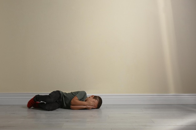 Garotinho fechando o rosto com as mãos no chão perto do espaço da parede amarela para texto Criança em perigo