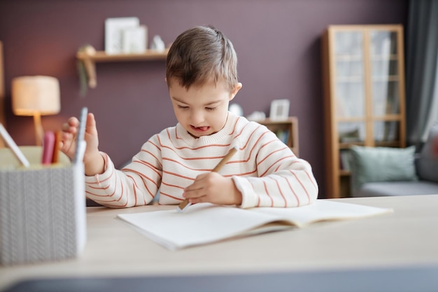 Garotinho focado com síndrome de down desenhando sentado à mesa em casa