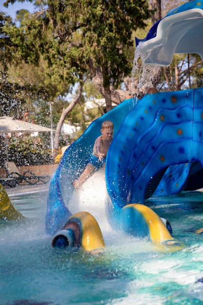 Garotinho fofo rola em um toboágua em um parque aquático Conceito de férias de verão diversão