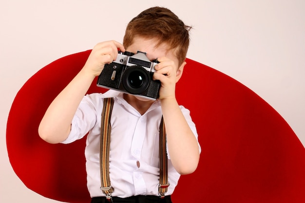 Garotinho fotógrafo em cadeira vermelha de estúdio com câmera de filme