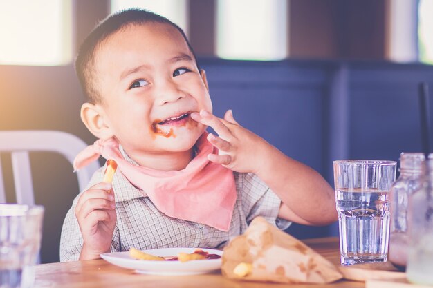 Garotinho gosta de comer batatas fritas com as mãos e molho no lábio