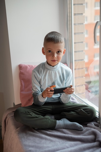 Garotinho jogando jogo para celular no smartphone sentado em uma vista superior do sofá Lazer infantil em vídeo doméstico