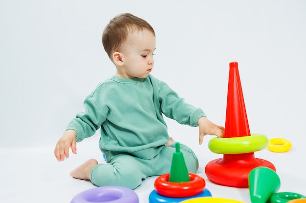 Garotinho jogando jogos educativos de lógica com pirâmide de plástico isolada no fundo branco Uma criança feliz brinca com um brinquedo educativo O bebê tem um ano e quatro meses de idade