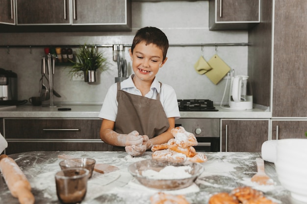 Garotinho na cozinha fazendo massa. menino ajuda a mãe na cozinha.