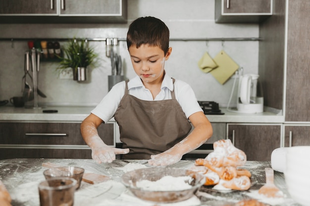 Garotinho na cozinha fazendo massa. menino ajuda a mãe na cozinha.