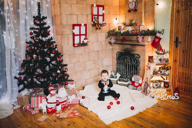 garotinho na decoração de Natal em um feriado segurando uma bola de brinquedo na árvore de Natal