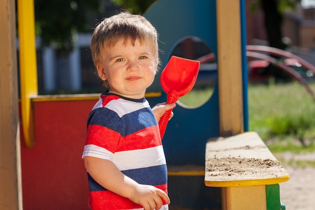 Garotinho no parque no playground. em uma camiseta listrada colorida com uma pá vermelha. foto de alta qualidade