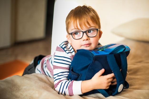 Garotinho nos óculos com síndrome de madrugada brincando com mochila