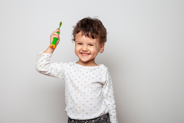 Garotinho, o garoto está de pijama e tem uma escova de dentes nas mãos. demonstração. Olhar sério de uma criança em um branco. procedimento de higiene pessoal.