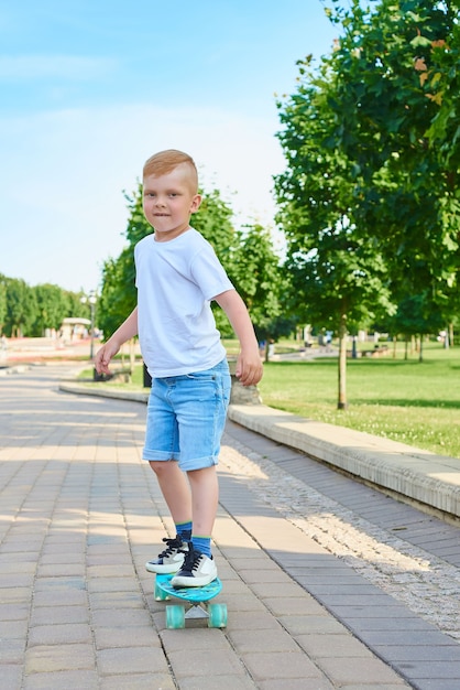 Garotinho ruivo andando de skate no parque no verão