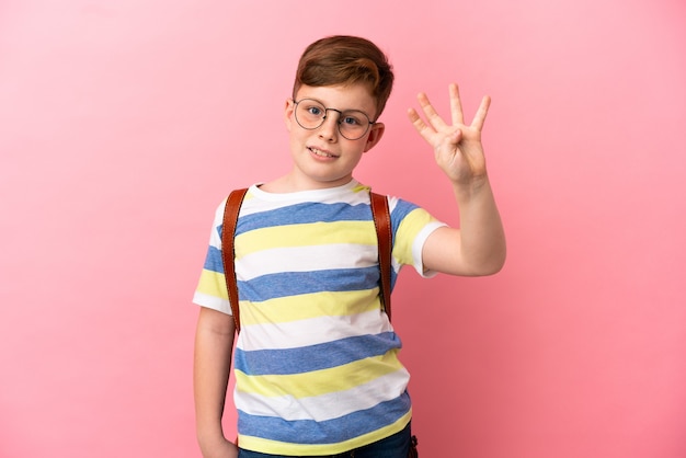 Garotinho ruivo caucasiano isolado em um fundo rosa feliz e contando quatro com os dedos