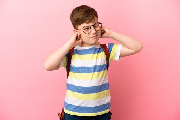 Foto garotinho ruivo caucasiano isolado em um fundo rosa frustrado e cobrindo as orelhas