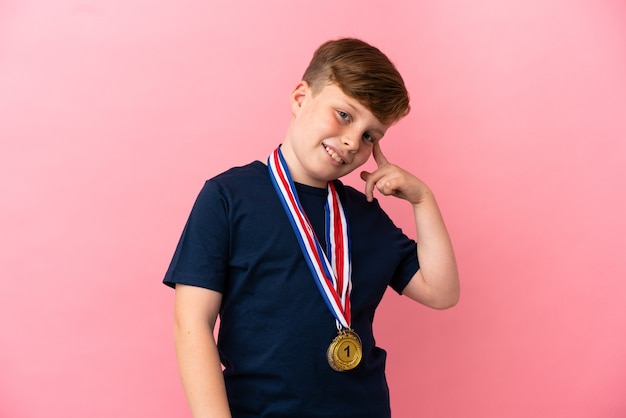 Garotinho ruivo com medalhas isoladas na parede rosa com a intenção de perceber a solução