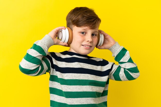 Garotinho ruivo isolado em um fundo amarelo ouvindo música